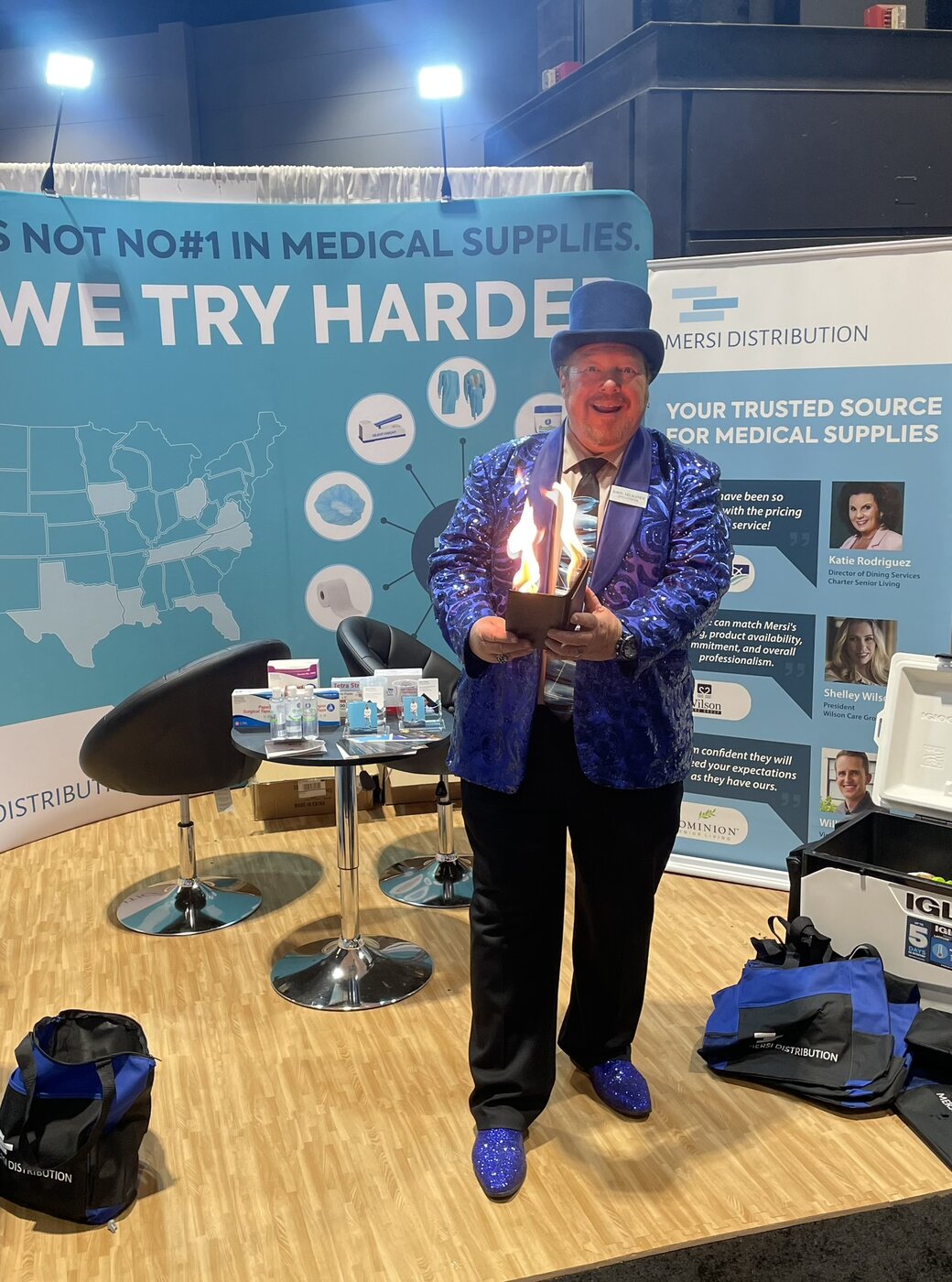 trade-show-magician-fire-illusion-booth-performance Trade show magician in a blue sequin jacket and top hat performing a fire illusion to draw booth traffic