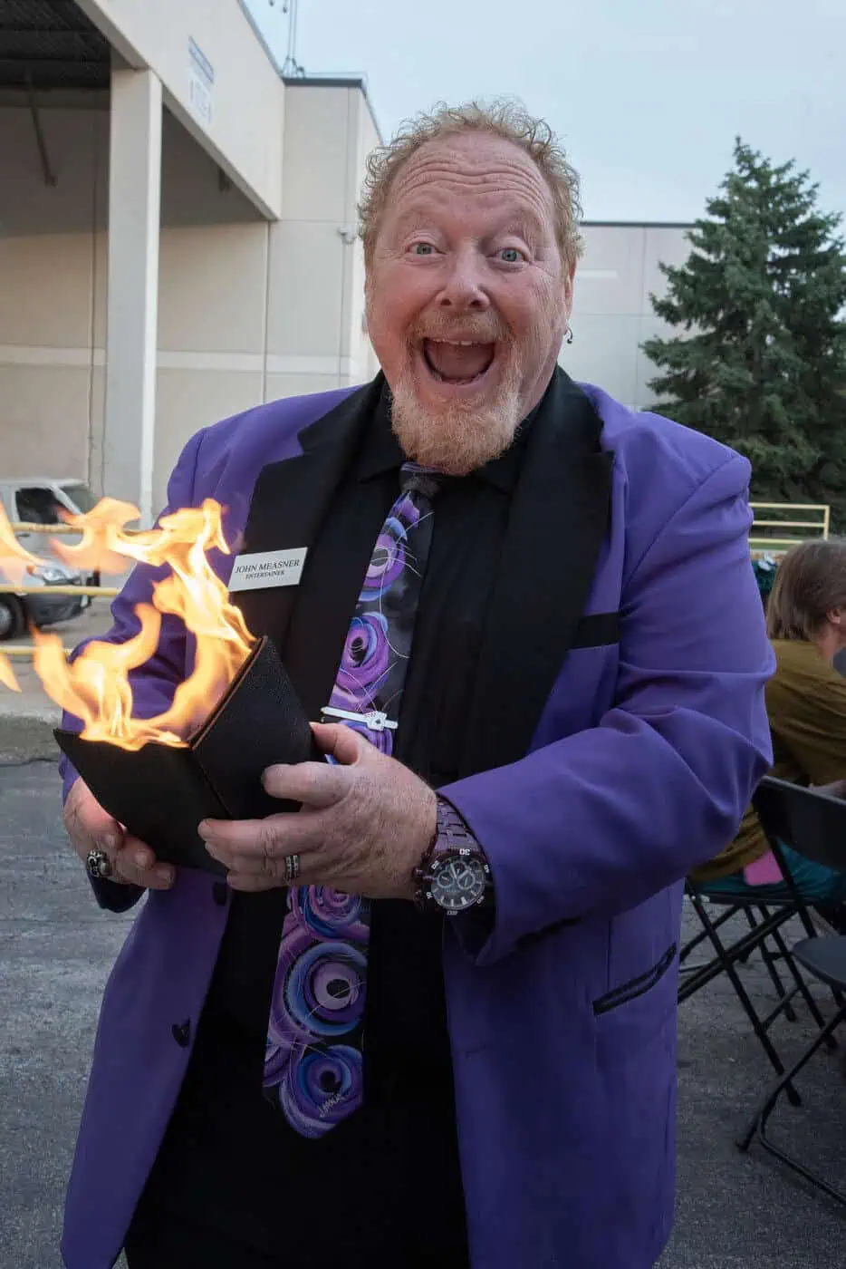 trade-show-magician-fire-wallet-trick-john-measner Trade show magician John Measner in a purple suit performing a fire wallet trick with an excited expression